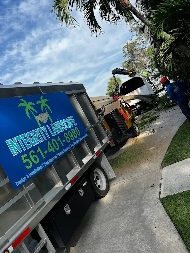 Integrity Landscape branded dump truck parked curbside with a wood chipper and crew actively working at a residential tree removal job