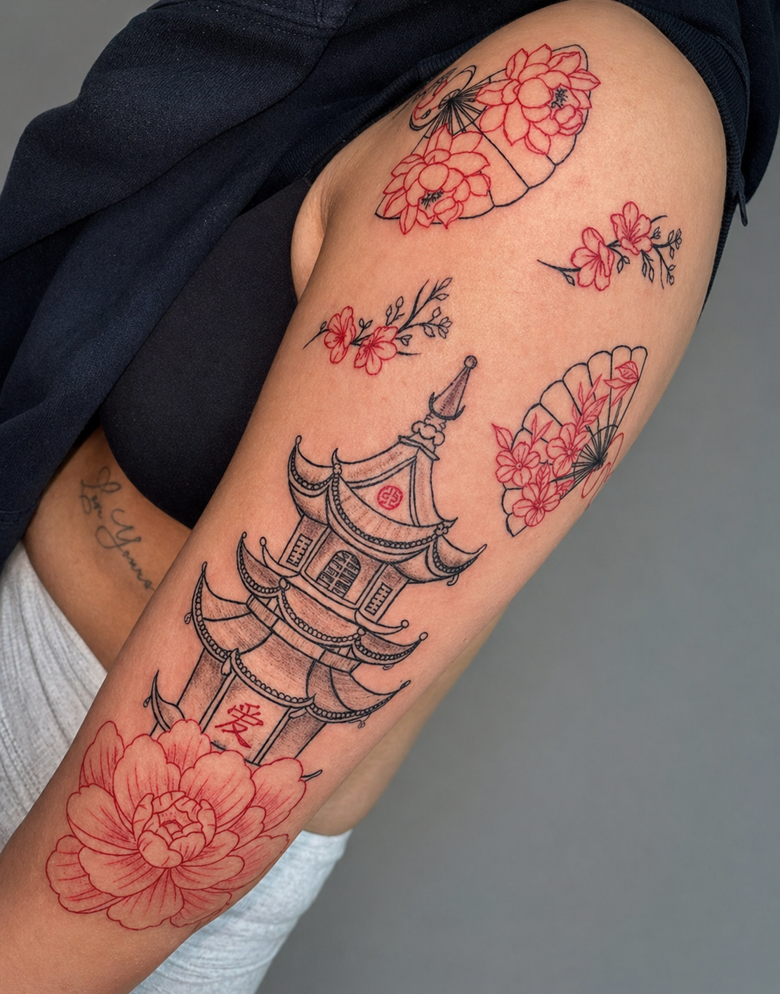 Arm tattoo of a Japanese pagoda with red peonies, hand fans, and cherry blossoms