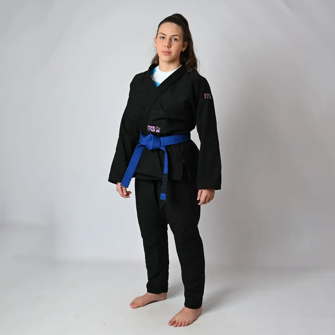 Kimono de Jiu-Jitsu Feminino In The Guard preto, corte anatômico com detalhe rosa, calça ripstop reforçada — atleta demonstrando caimento com faixa azul