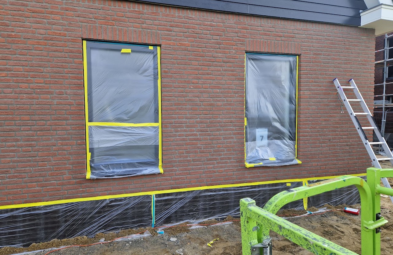 Bakstenen gevel van een nieuwbouwwoning met kozijnen afgeplakt met folie en gele tape