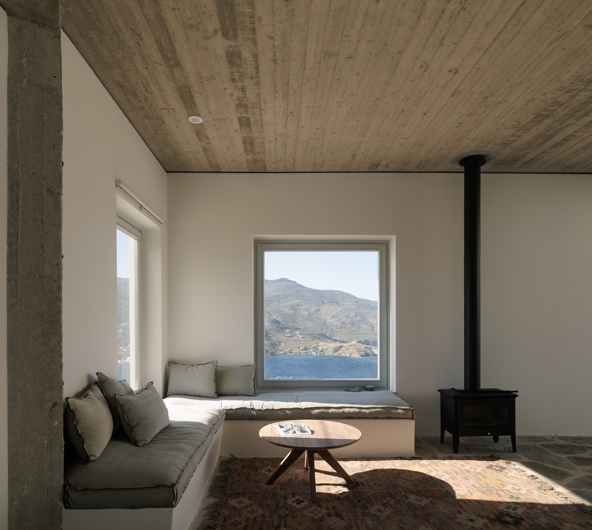Living room with concrete ceiling, built-in window seat and wood stove framing the bay