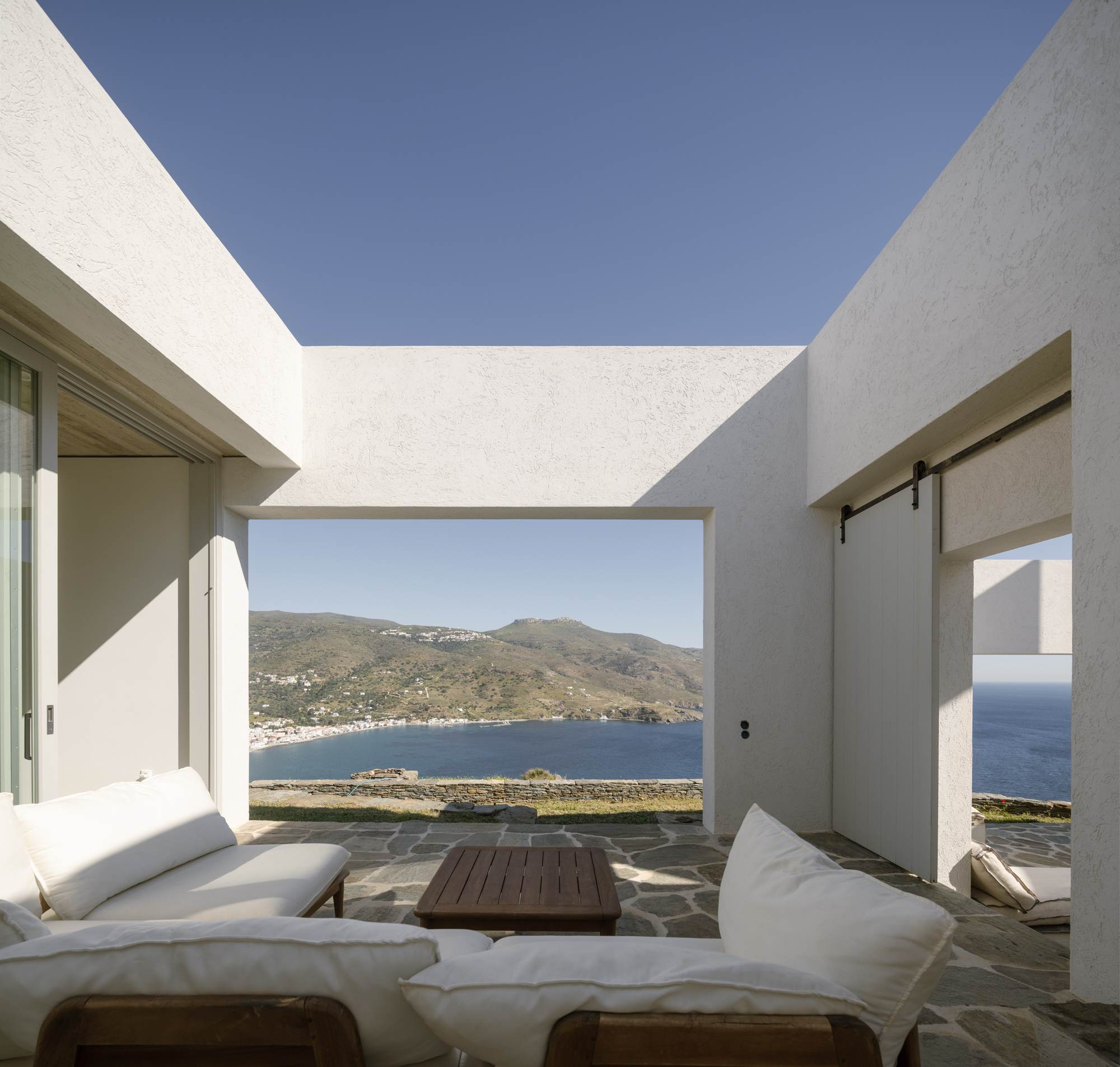 Shaded terrace with white lounge seating overlooking Korthi village and bay