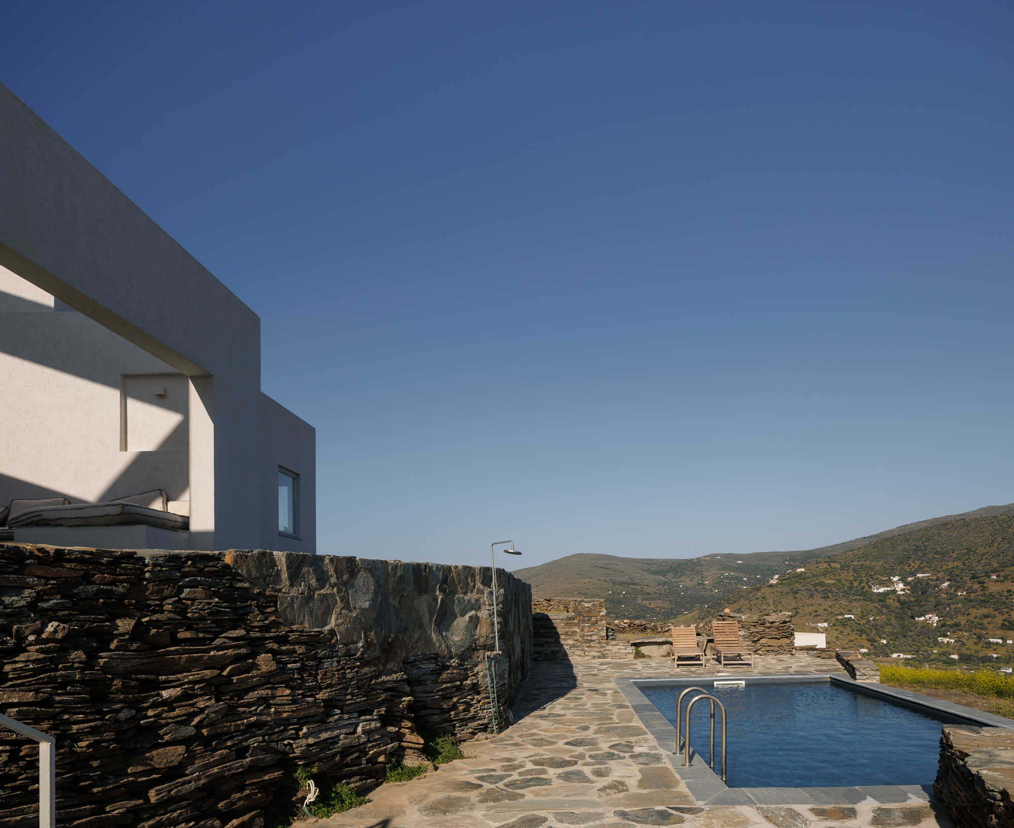 Pool with outdoor shower and dry stone wall under a clear blue sky