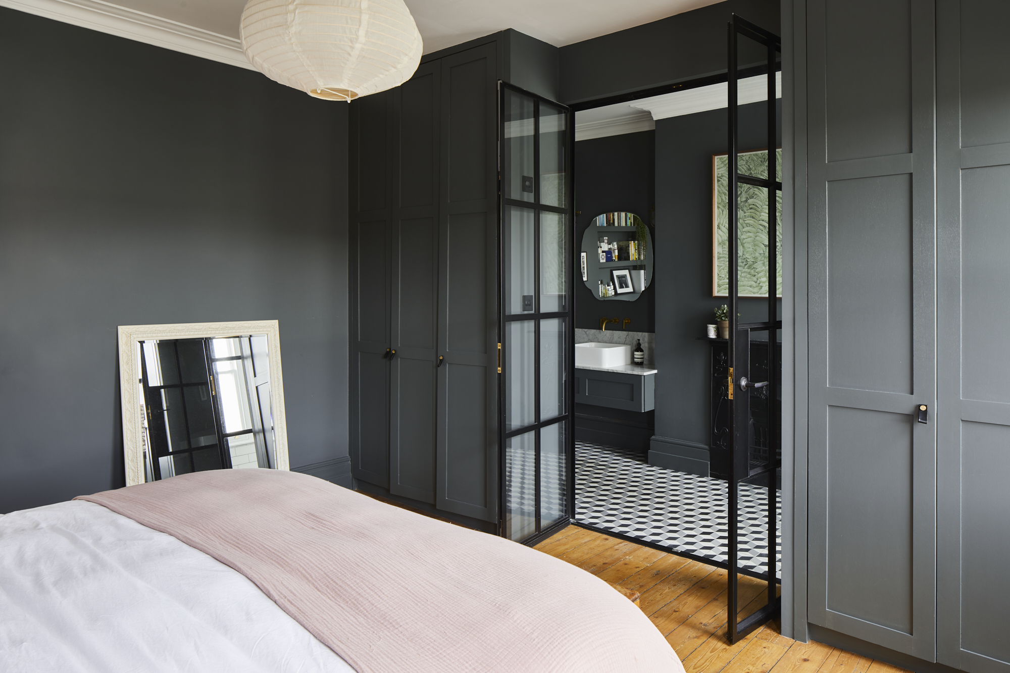 Modern bedroom with dark grey walls, built-in wardrobes, and glass-paneled door leading to an en-suite bathroom