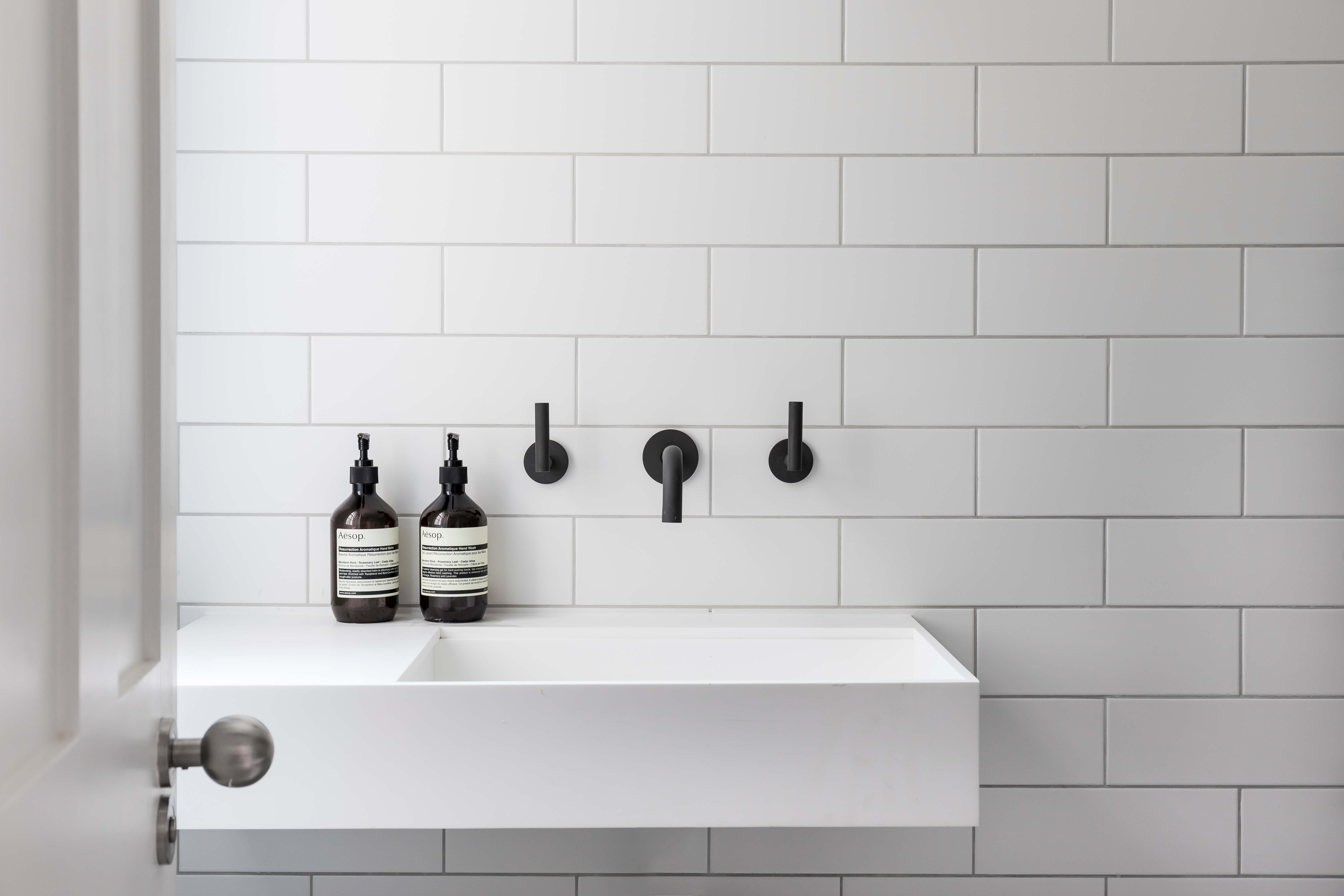 Minimalist white floating sink with matte black fixtures against white subway tiles