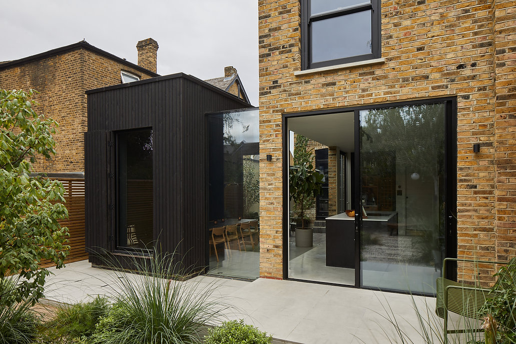 Exterior of London house extension with yellow brick and black cladding featuring large glass doors