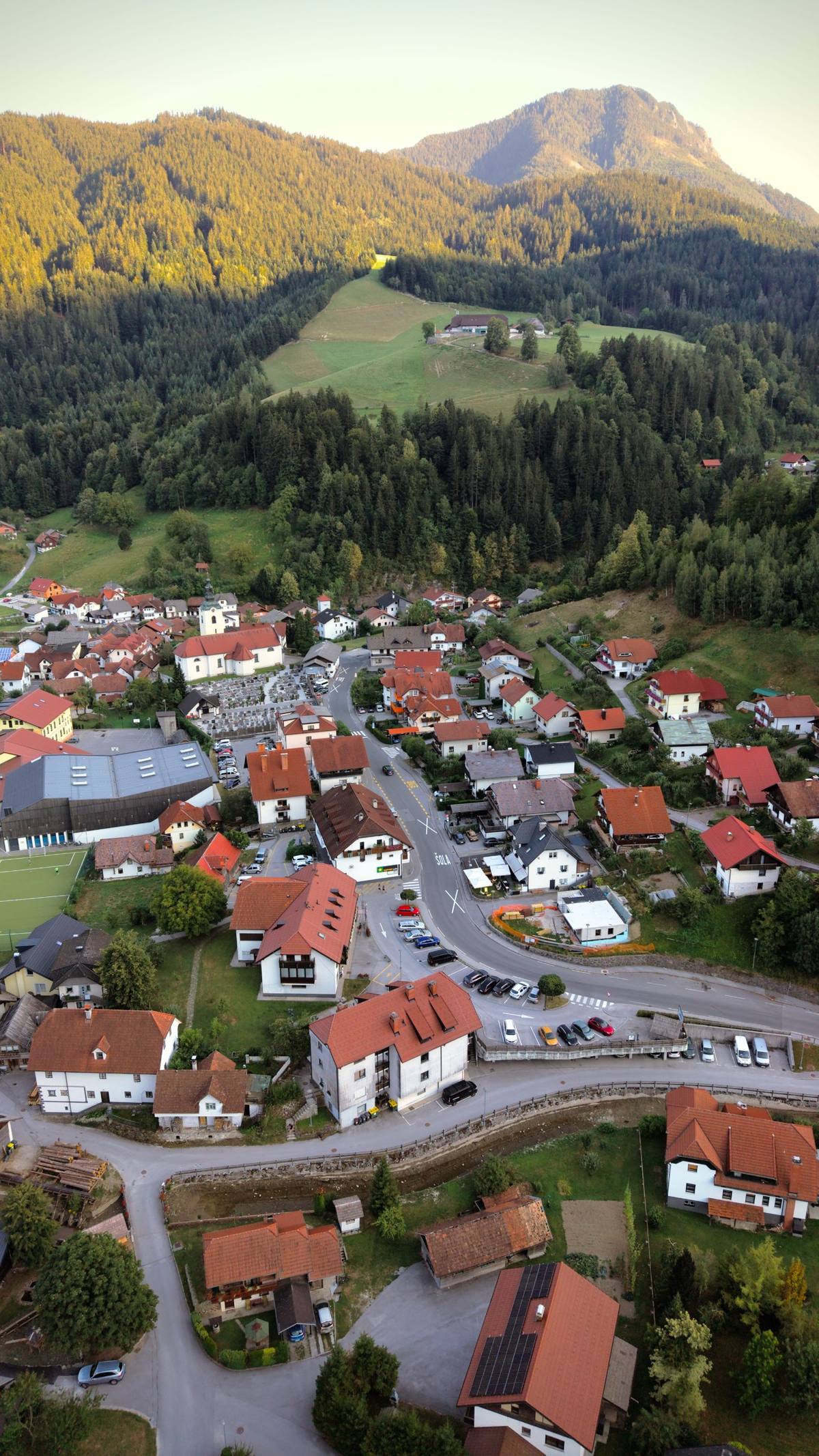 Aerial view of the village of Luče ob Savinji with its church, red-roofed houses and forested mountains