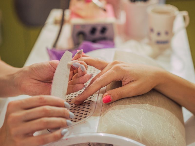 Manicure technician filing a client’s polished nails at a workstation.