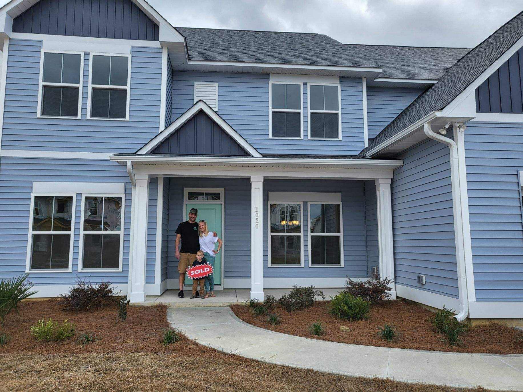 Family with sold sign in front of blue coastal home