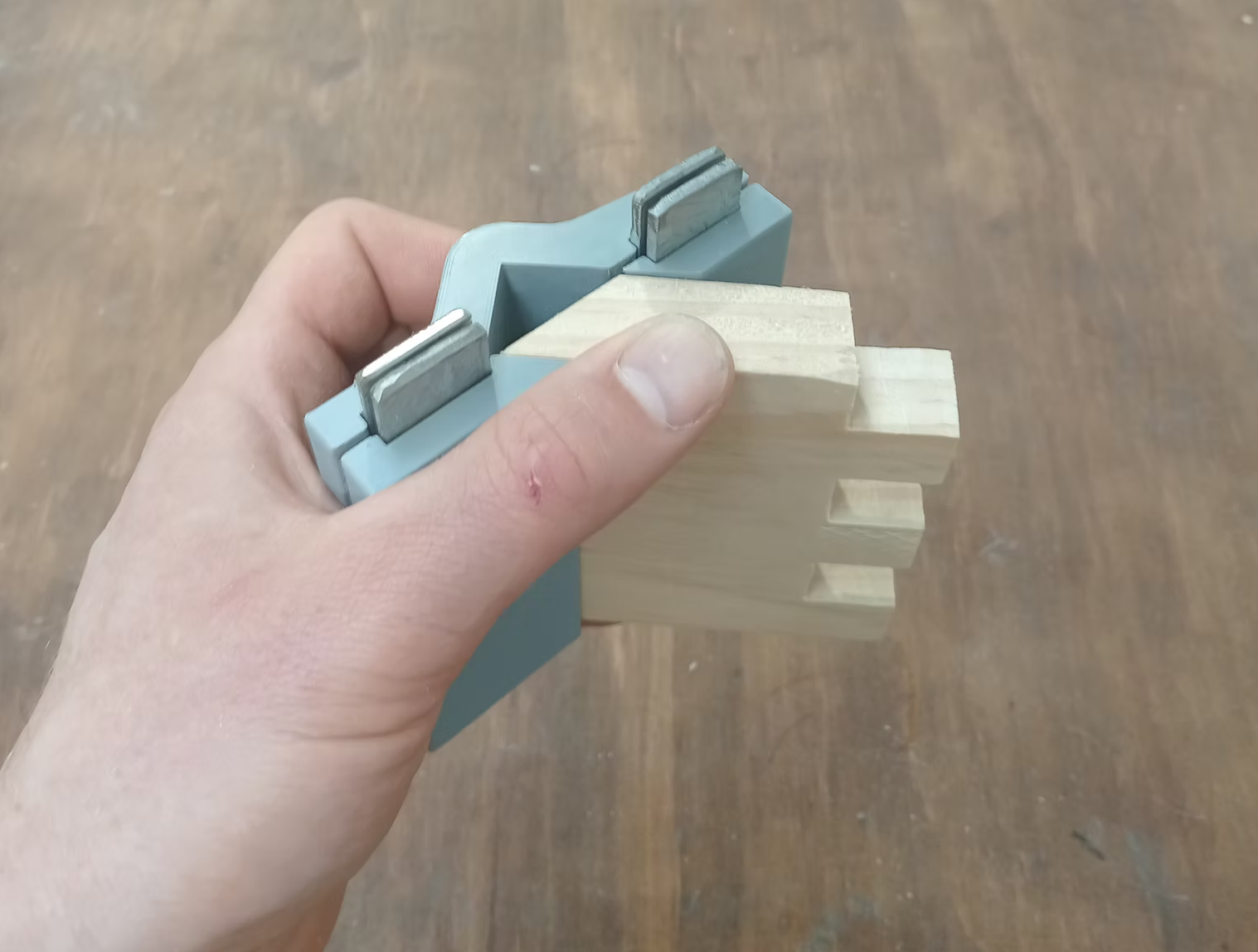 Hand holding a teal 3D printed mitre jig against a finger-jointed timber piece