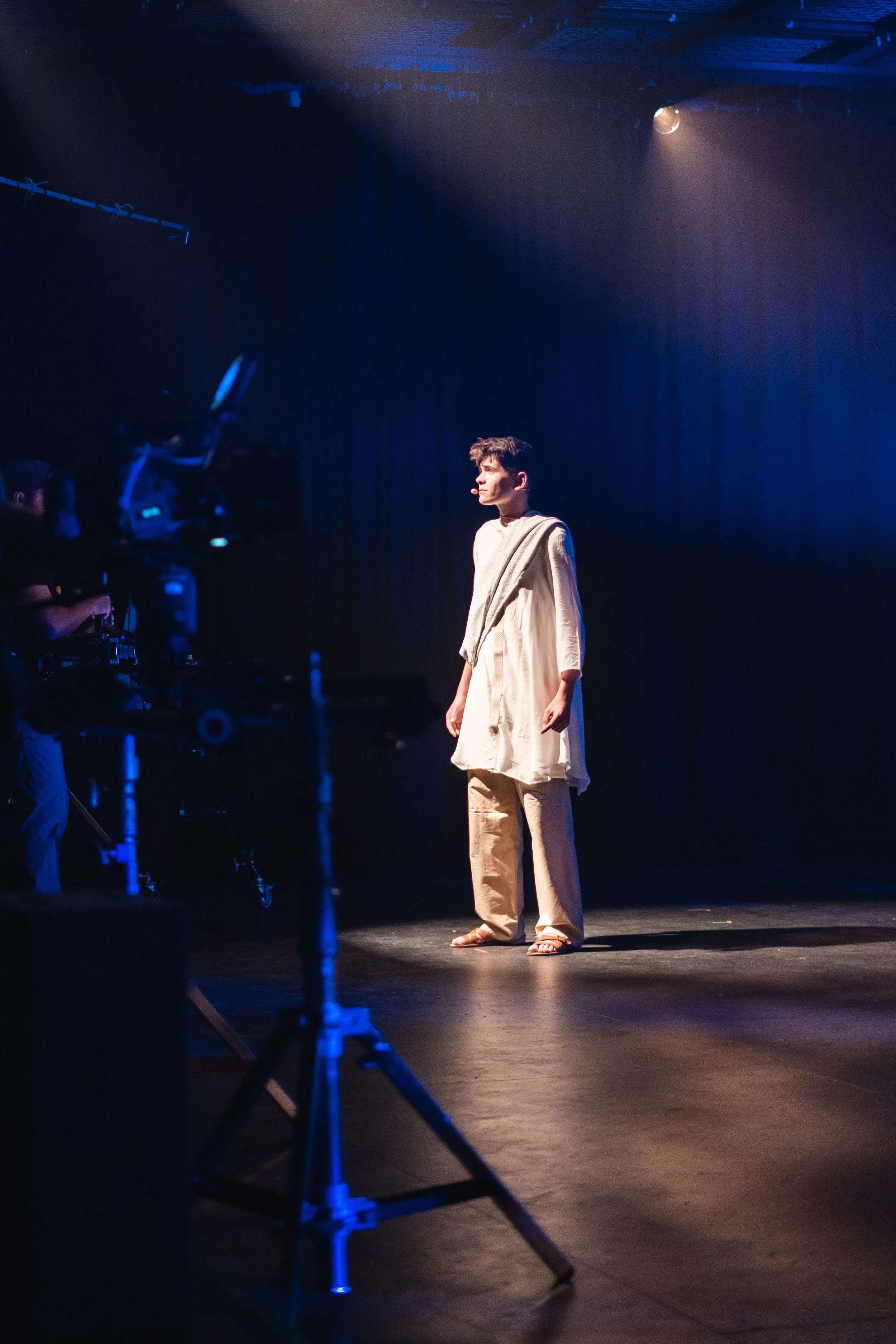 A performer standing alone in a spotlight on a darkened stage
