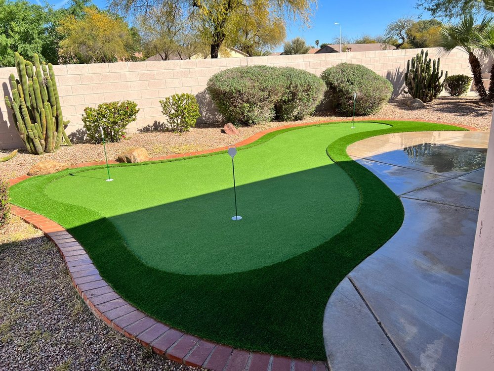 Custom two-tier putting green bordered by desert landscaping and pool edge