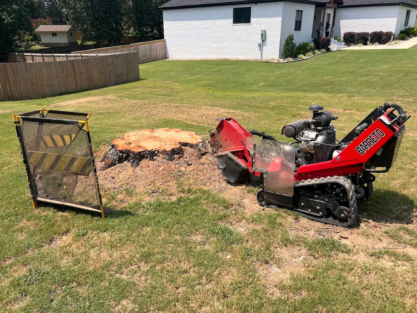 Barreto stump grinder positioned next to large tree stump with safety barrier in residential yard