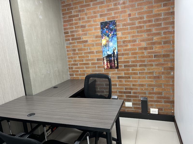 Oficina 17 compacta con escritorio en L, silla ergonómica y pared de ladrillo en El Poblado, Medellín