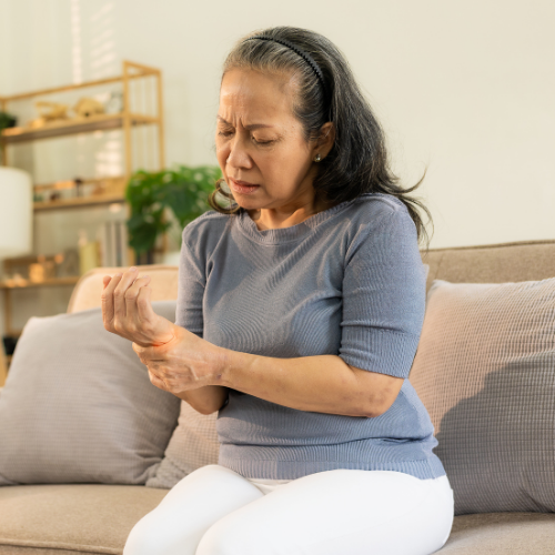 An older woman sitting on a couch holding her wrist, indicating joint pain
