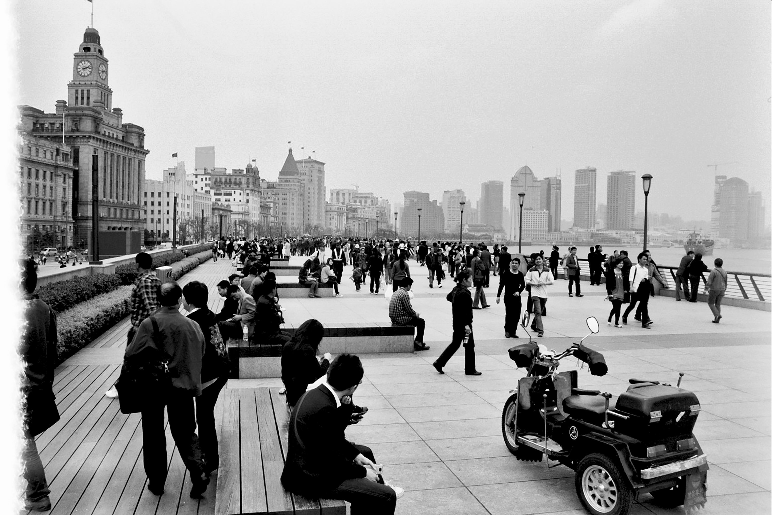 Crowded Shanghai Bund waterfront promenade with historic clock tower, colonial architecture, modern skyline, and pedestrians