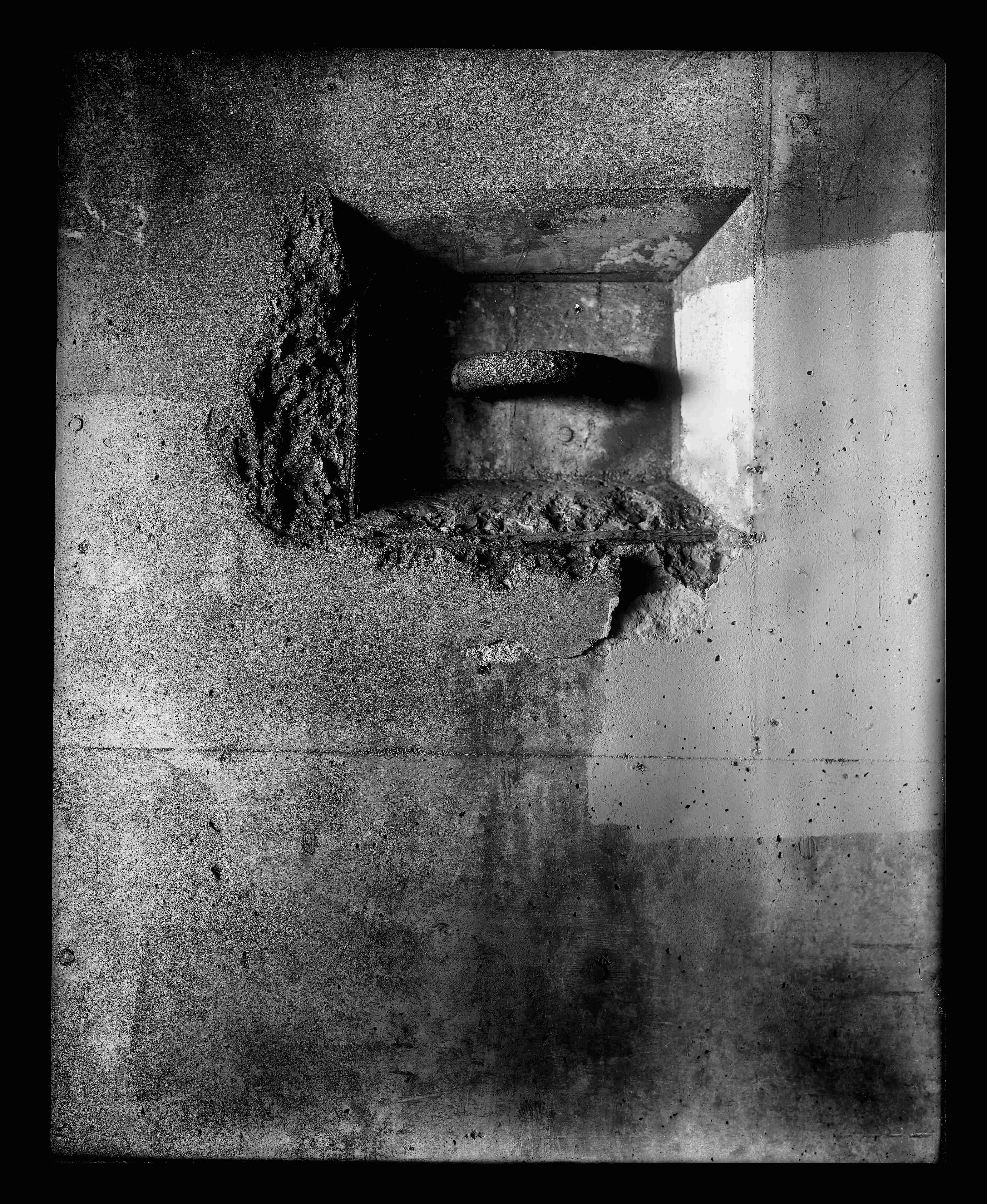Deteriorated concrete wall with large opening revealing rusted metal pipe and architectural decay