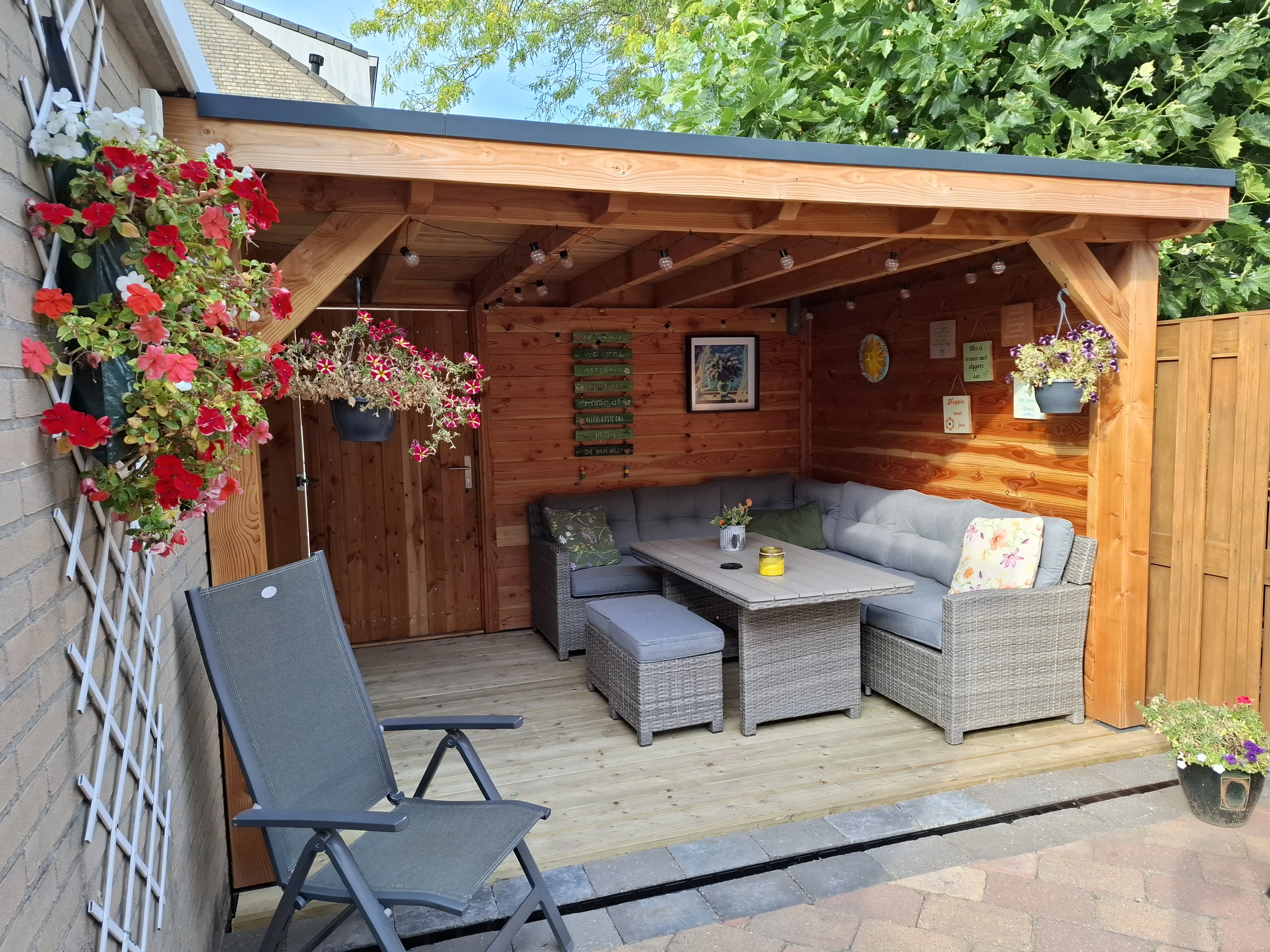 Veranda met loungeset en bloeiende hangplanten - Tuinaanleg Zoetermeer