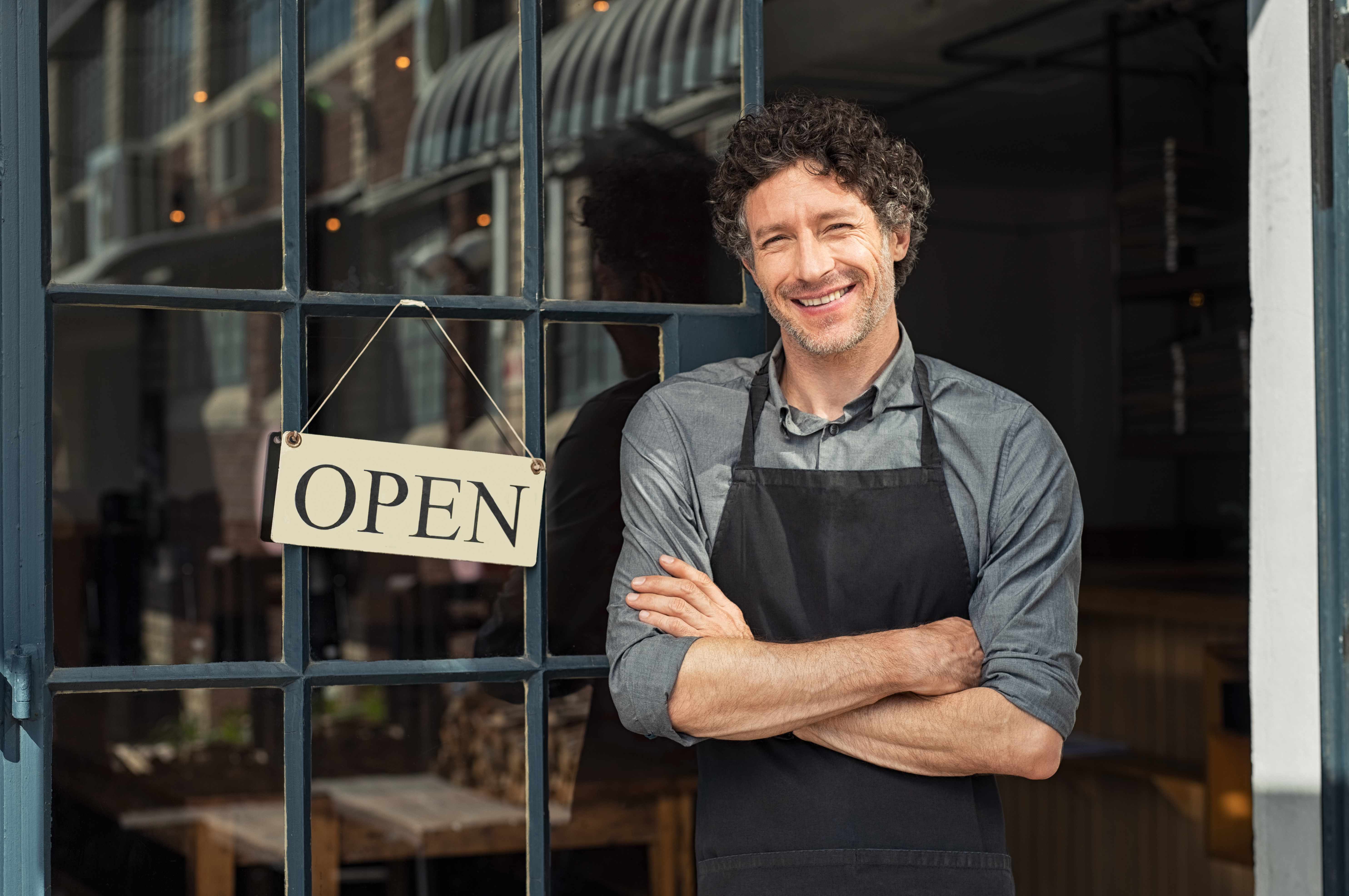 A small business owner standing proudly in the open doorway of his shop