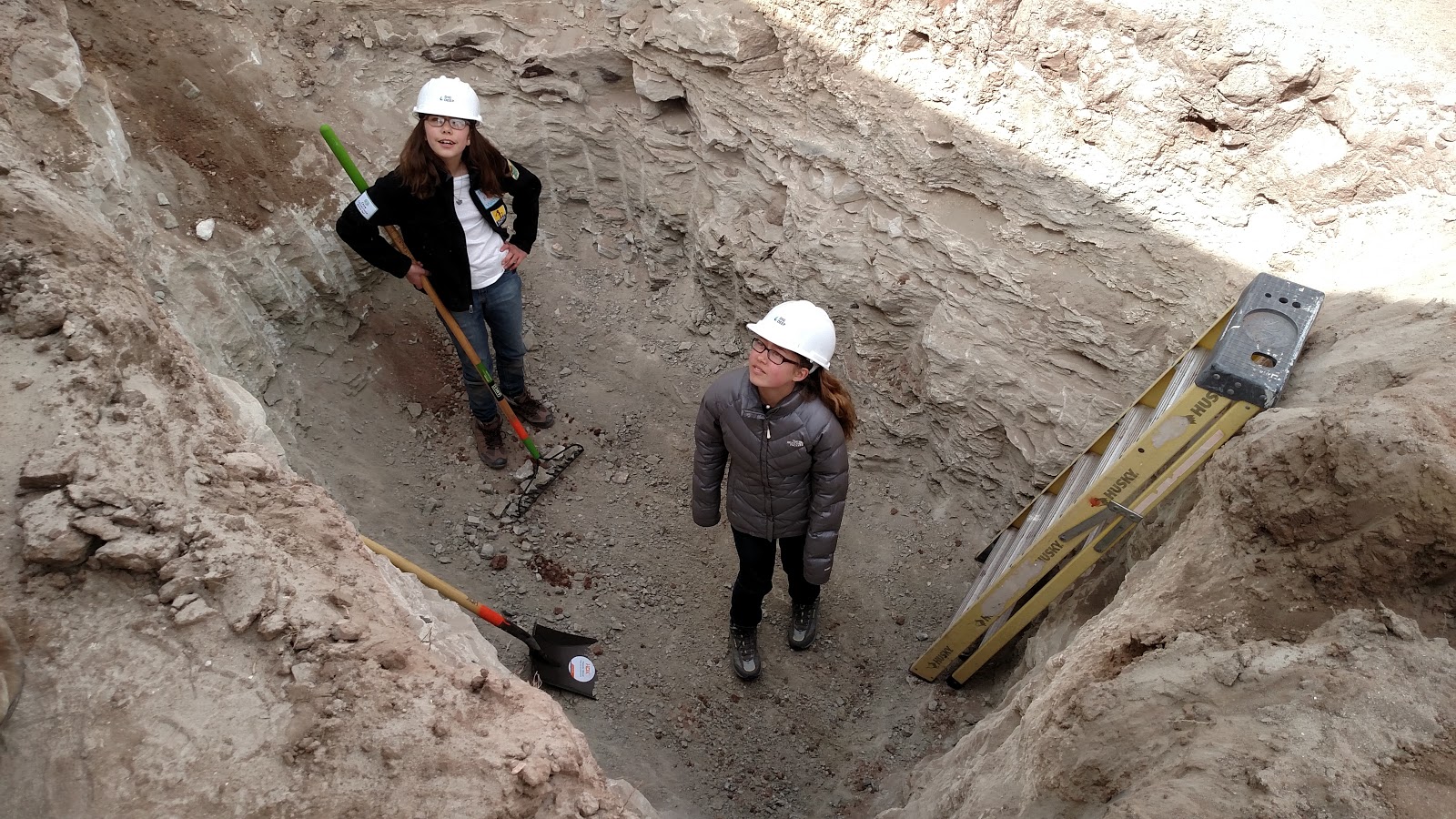 Two girls in hard hats standing in a dig trench on the Navajo Nation
