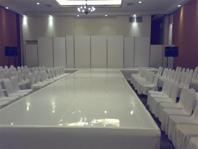 Pasarela blanca larga con sillas blancas a los lados en salón interior con decoración púrpura