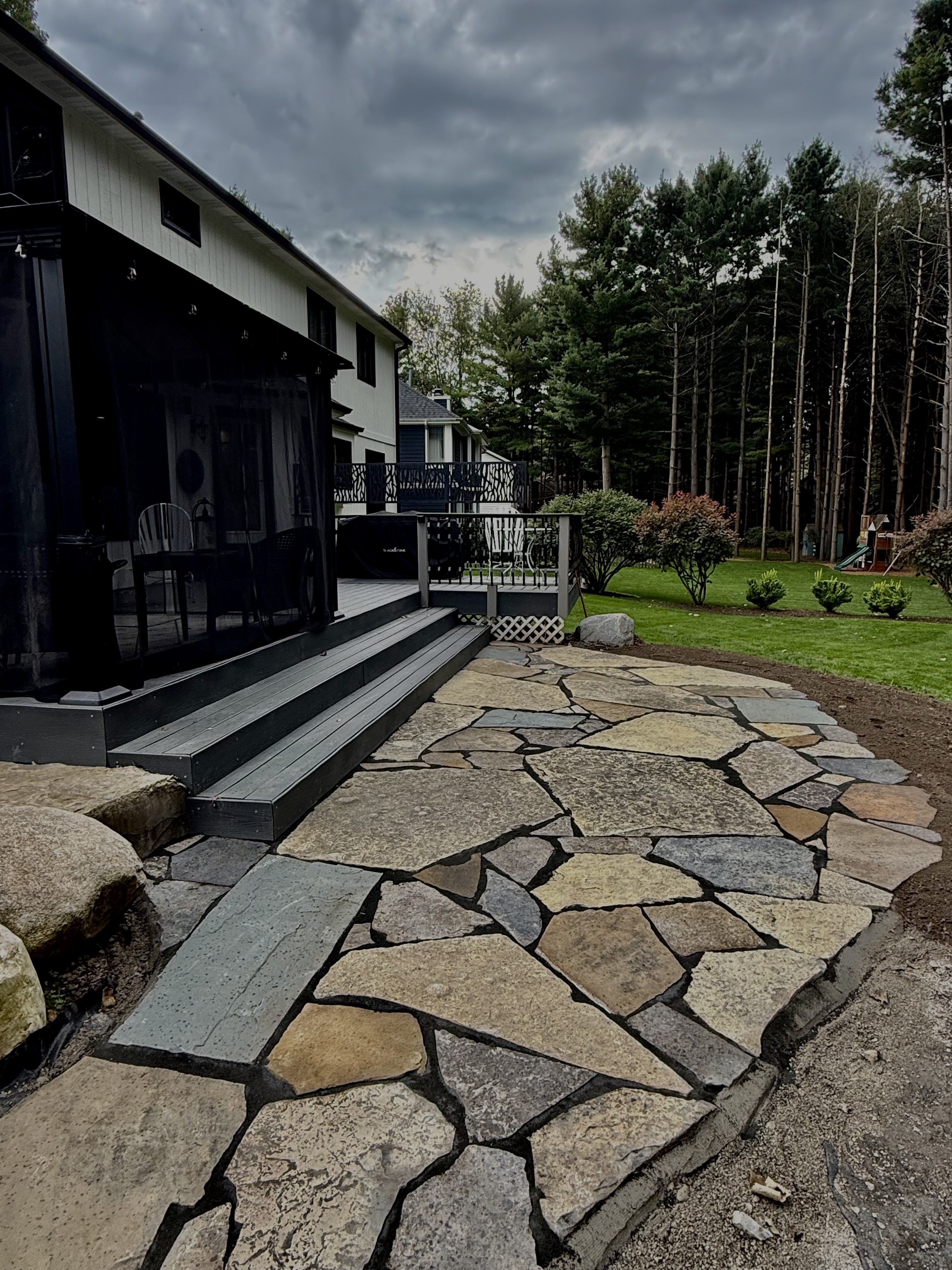 Full view of irregular flagstone patio with deck transition and stormy sky backdrop