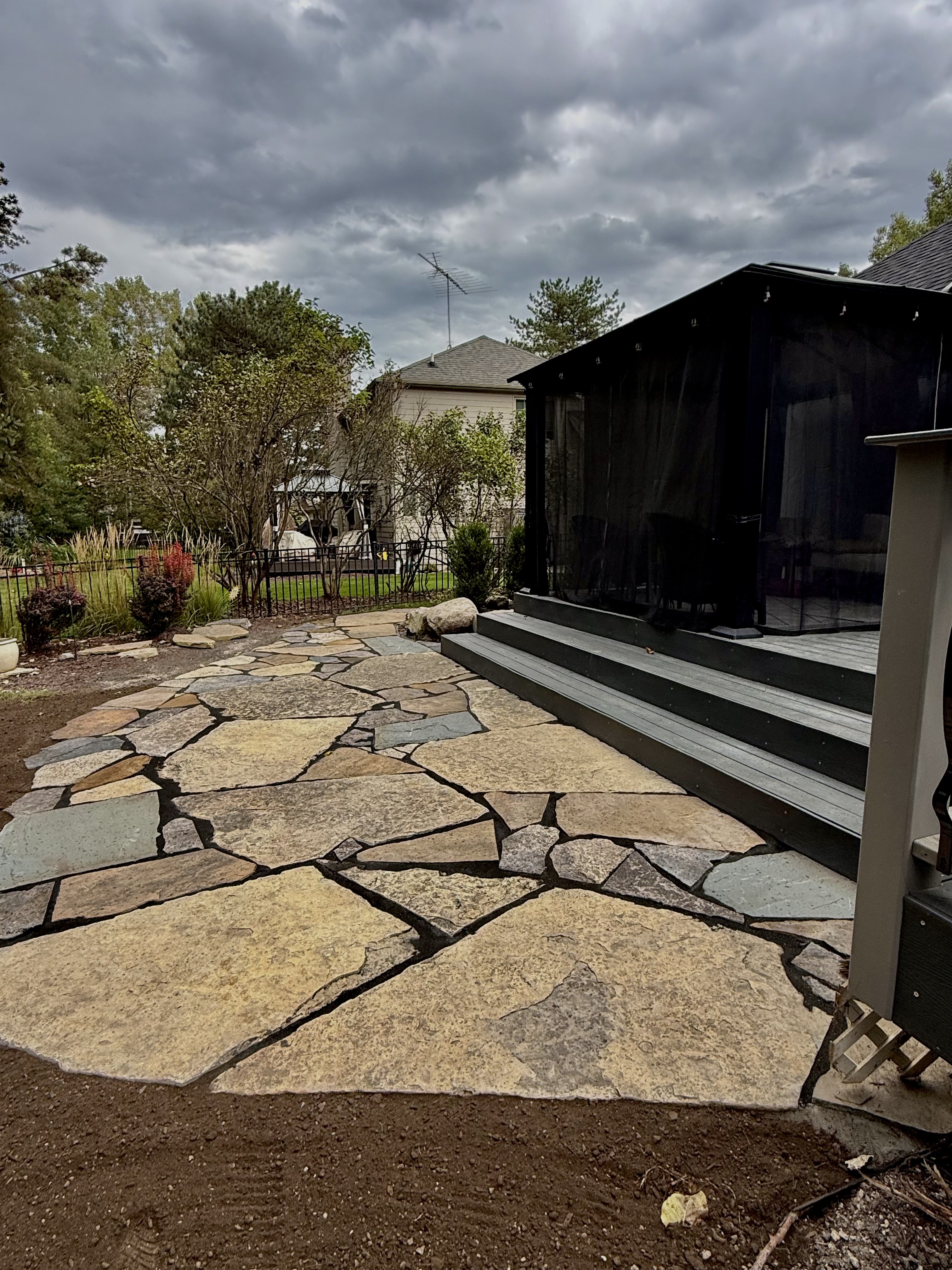 Wide angle of natural stone patio alongside black screened porch structure