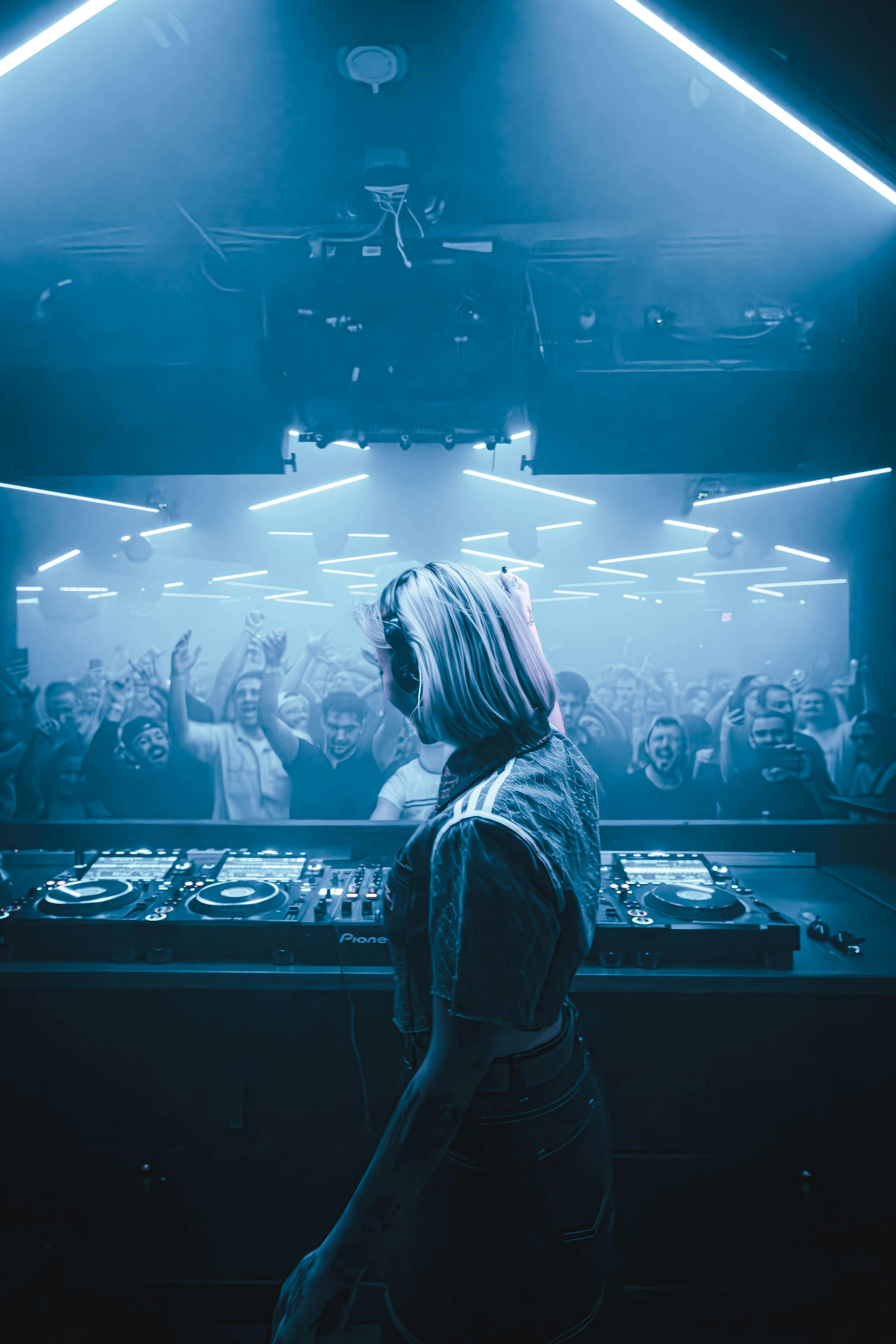 DJ facing crowd with hands in the air under blue lights