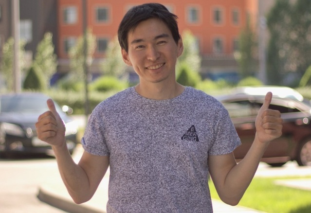 A person giving thumbs up and smiling at the camera, wearing a gray t-shirt with a triangle logo