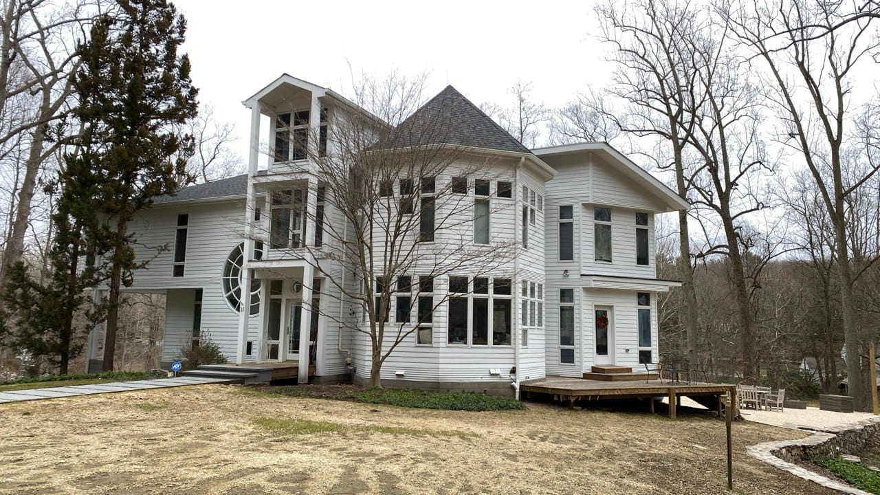 Gutter installation on gray colonial with round tower and wooden deck — wooded Connecticut property