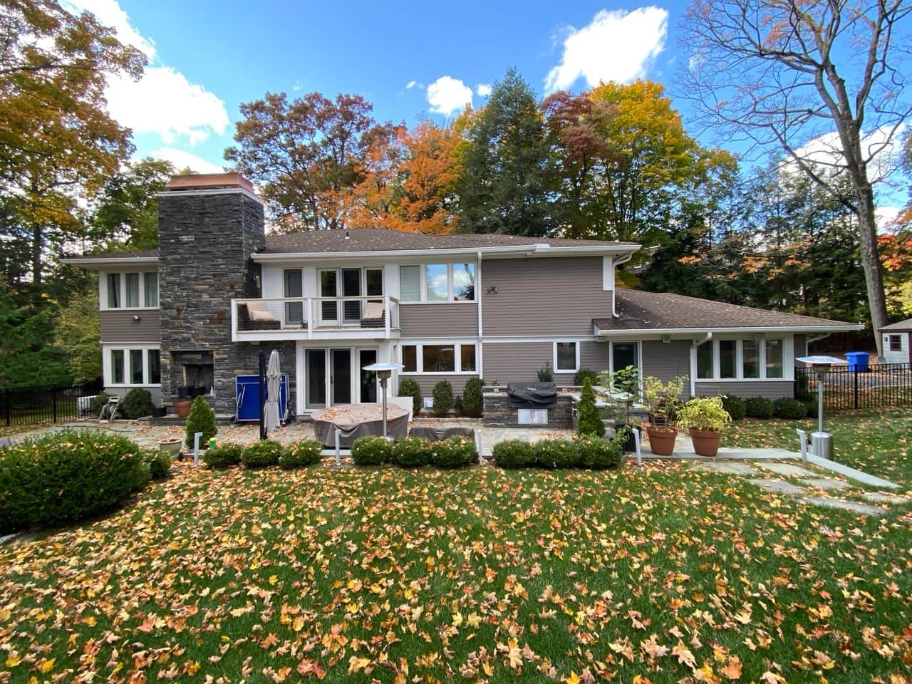 New gutter system on gray two-story home with balcony and stone patio — autumn Westchester County
