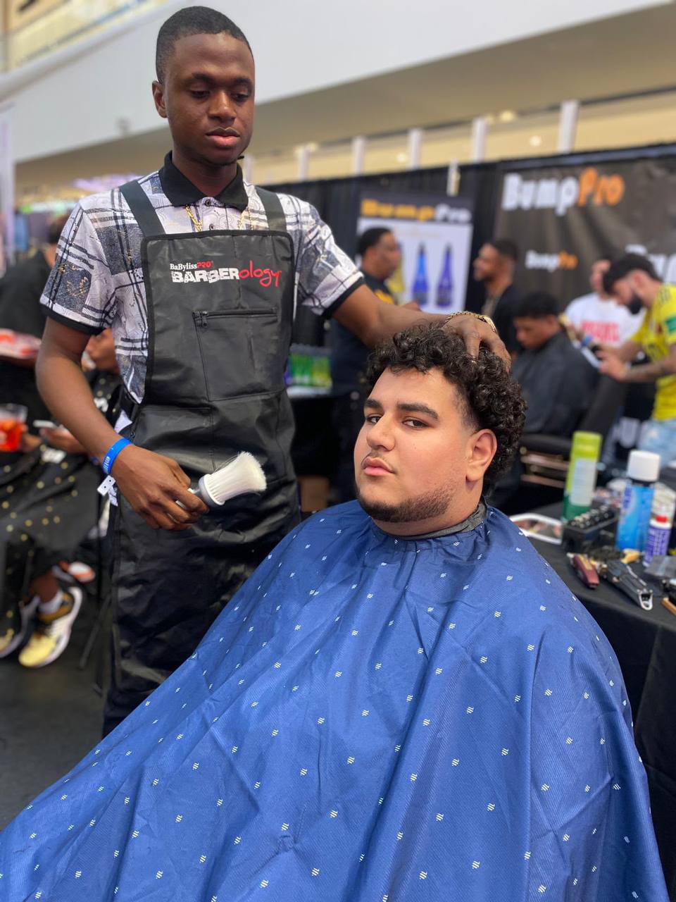 Professional barbering session at Babyliss PRO event with blue cape