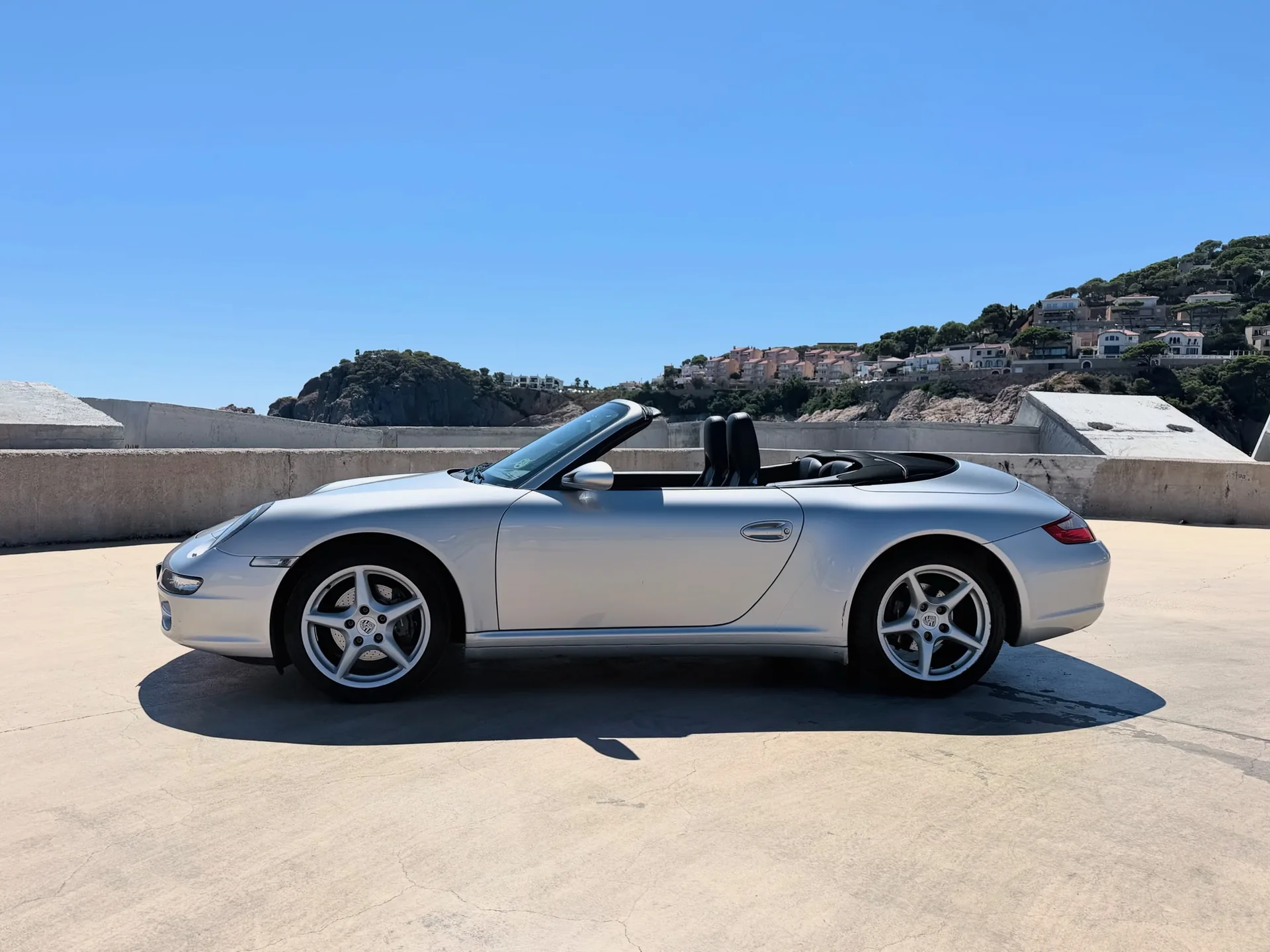 Complete side profile of the silver Porsche 911 Carrera 4 Cabriolet with the roof down
