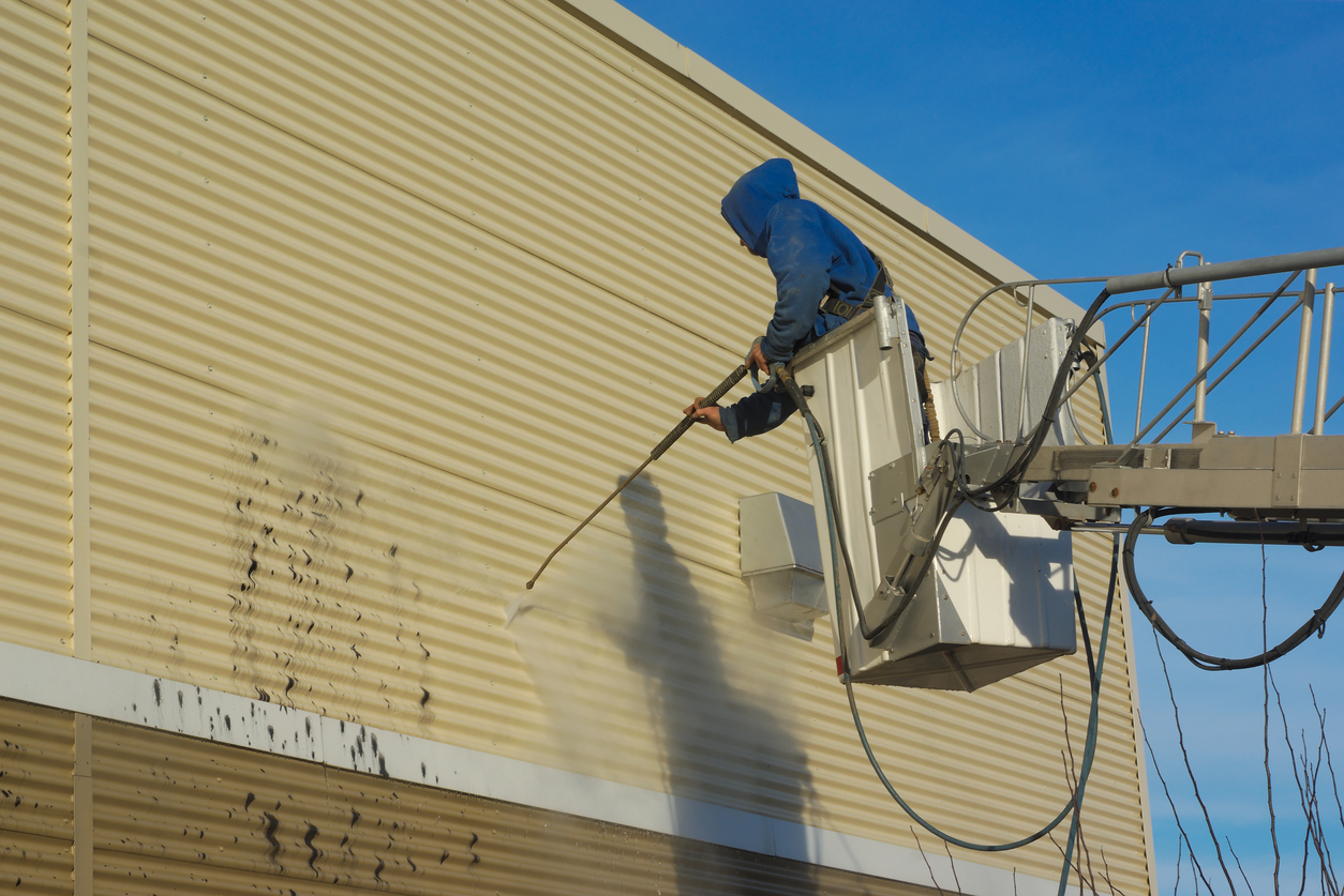 Worker in an elevated lift pressure washing a commercial metal building exterior