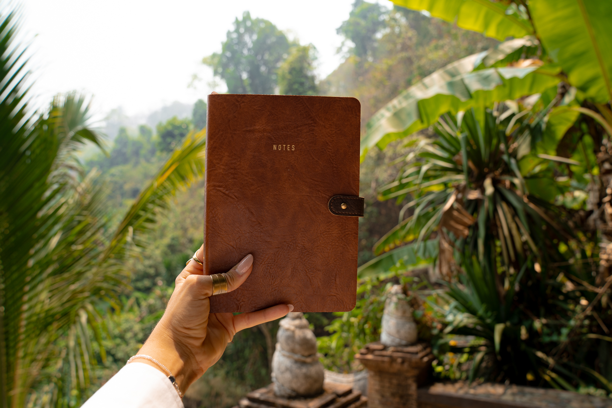 Hand holding leather journal in tropical setting