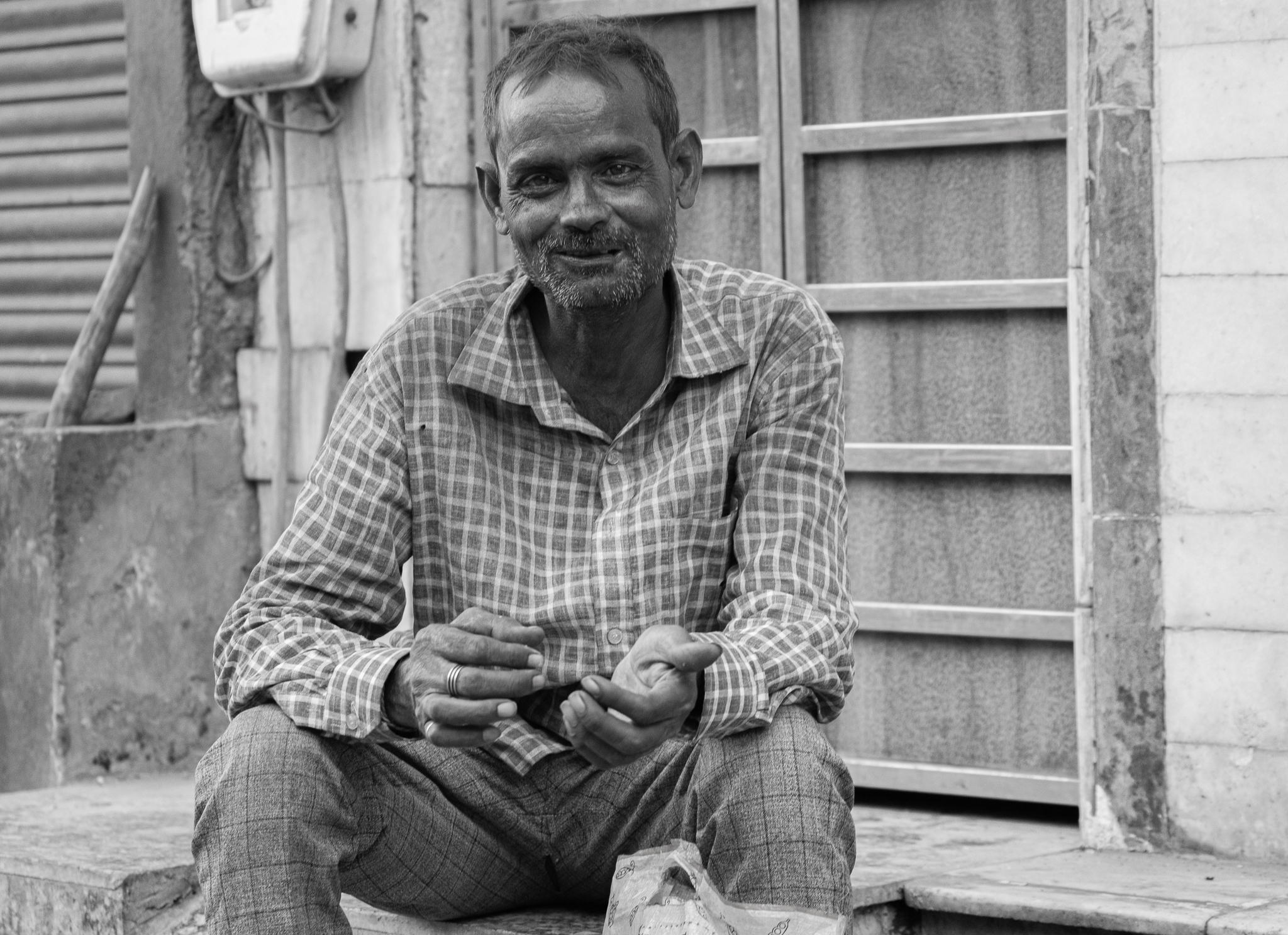 Smiling Indian man sitting on steps in plaid shirt