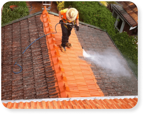 Worker cleaning a tiled roof with controlled washing equipment