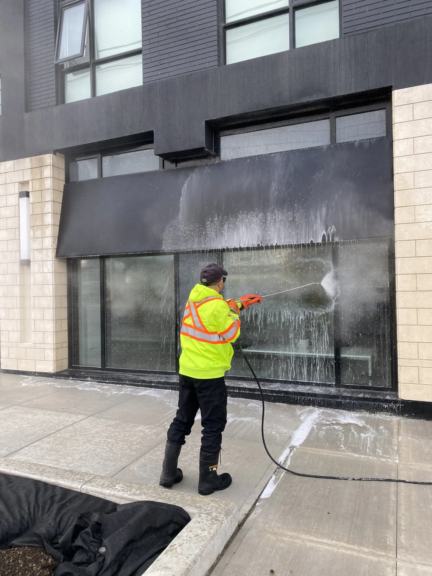 Commercial cleaning worker pressure washing a dark storefront facade and windows