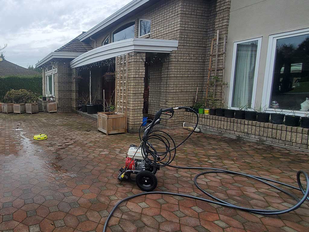 Professional pressure washer and hoses staged on wet pavers