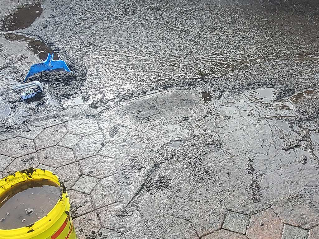 Partially cleaned paver surface showing heavy soil and wash water