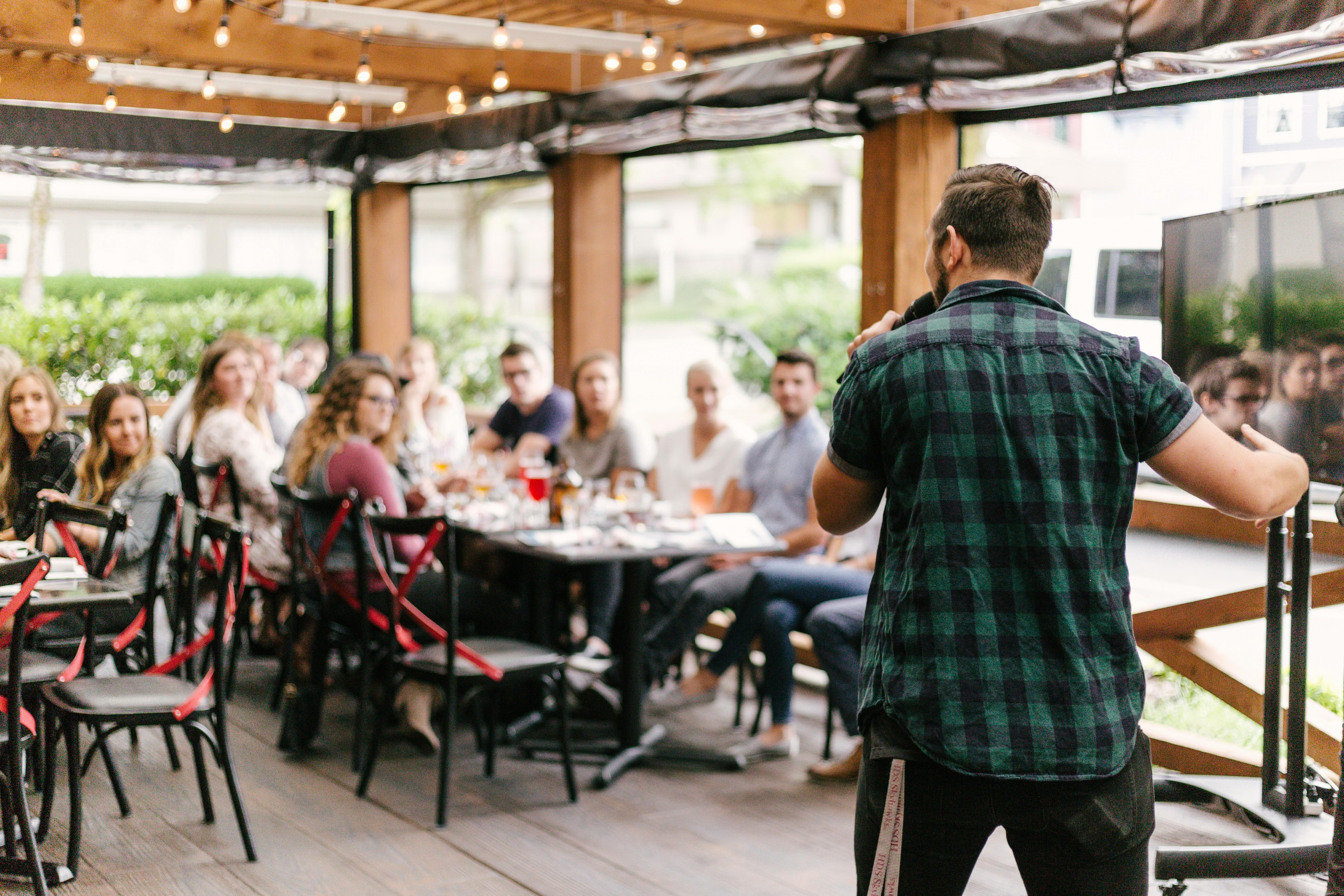 Community members gathered at a meetup, with a speaker addressing the group in a warm, well-lit venue