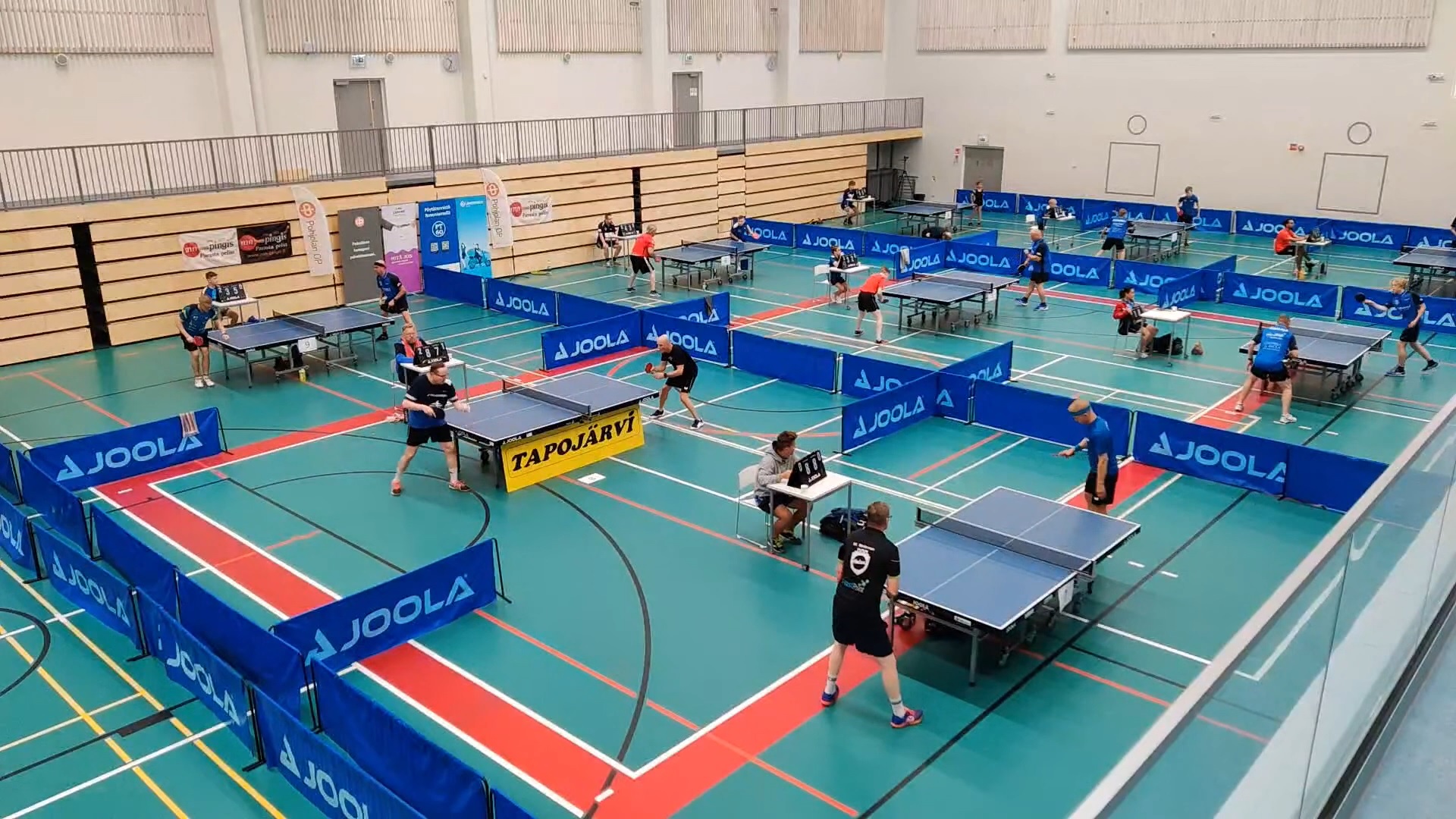 PT-60 table tennis players competing across rows of tables at a Finnish tournament hall