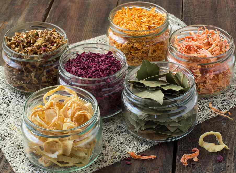 Glass jars containing various dehydrated vegetables, herbs, and leafy greens