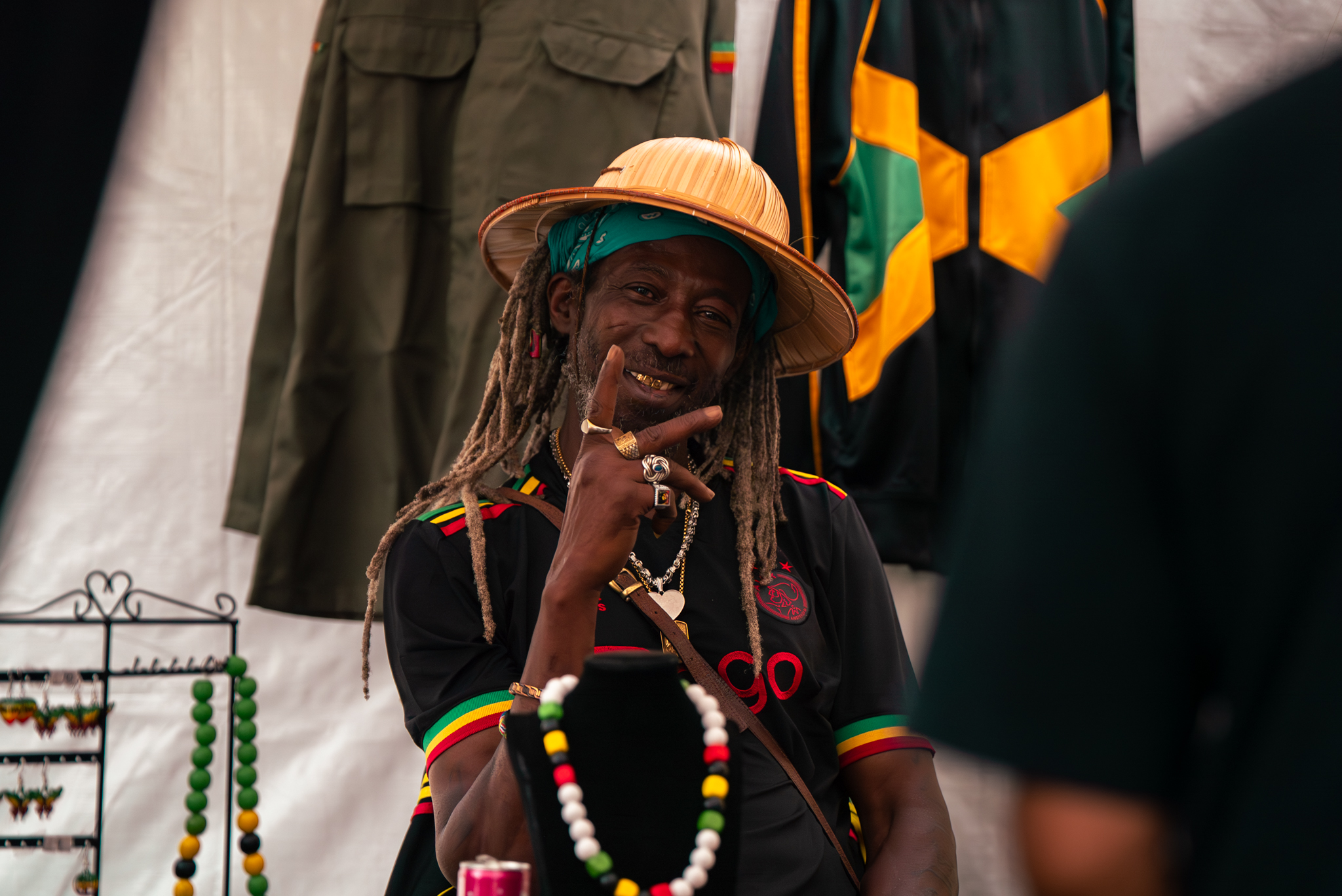 Man met dreadlocks en strohoed poseert bij kleding en sieraden op Rastaplas 2025