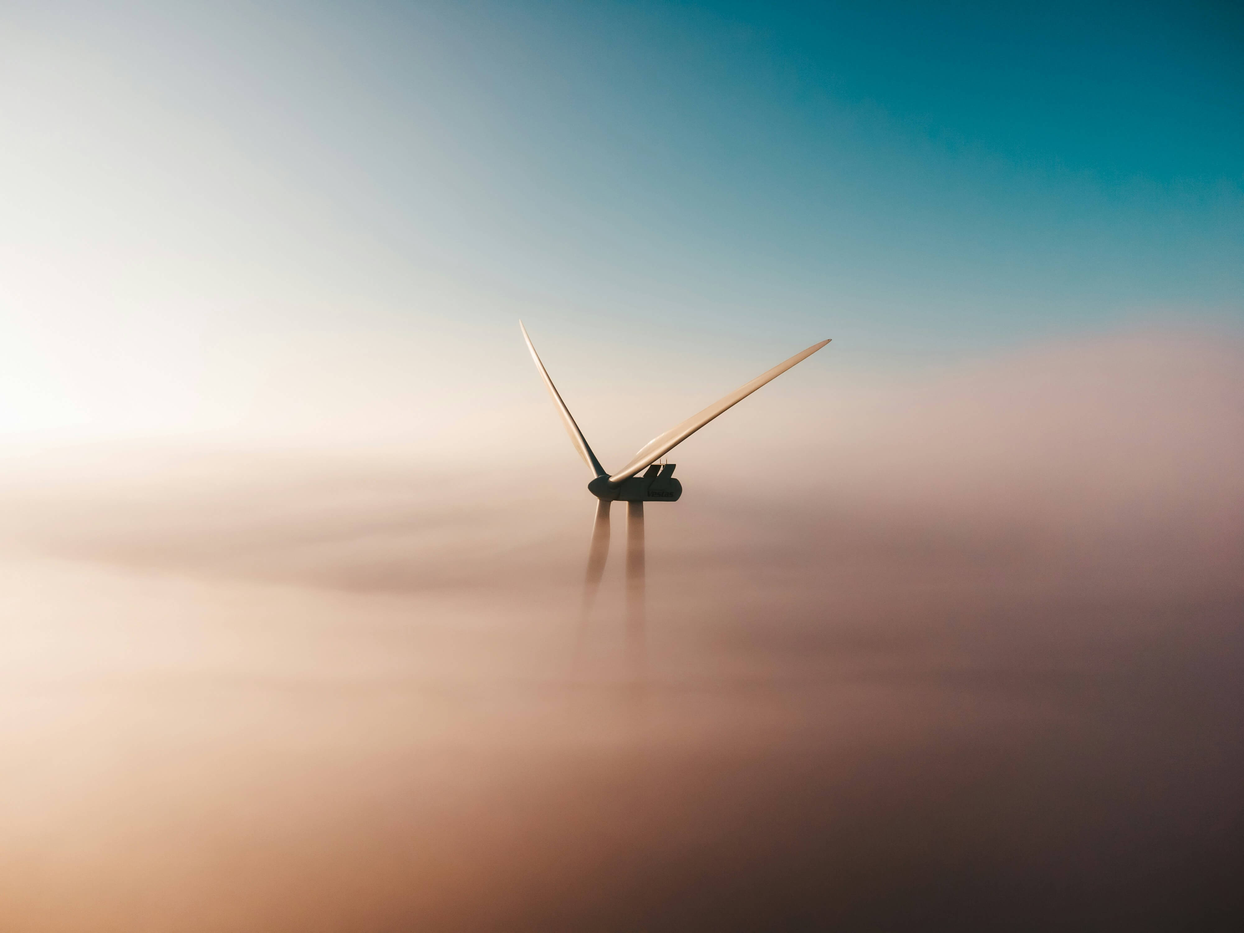 Offshore wind turbine rising through low fog at dusk