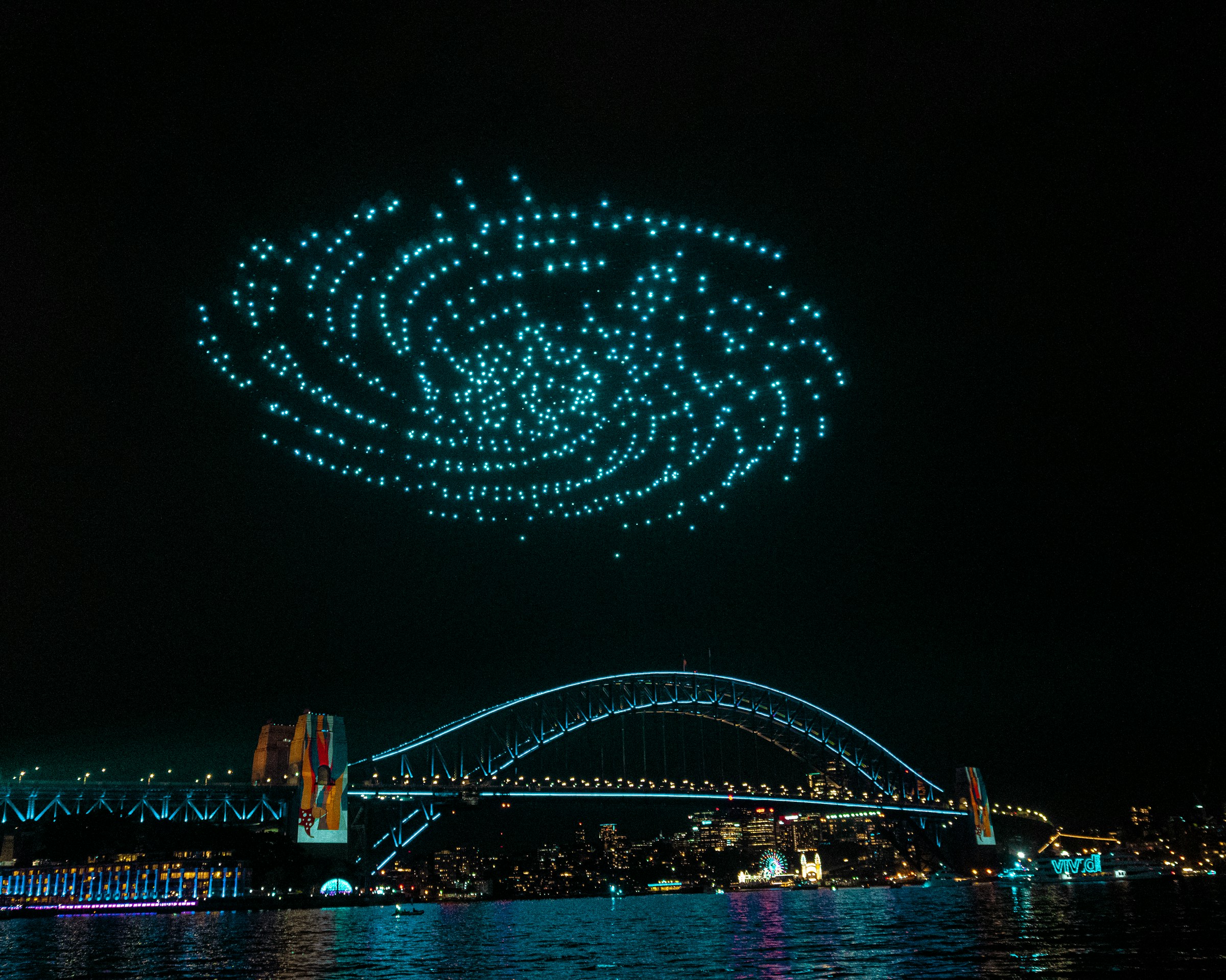 Drone light show forming spiral pattern over Sydney Harbour Bridge at night
