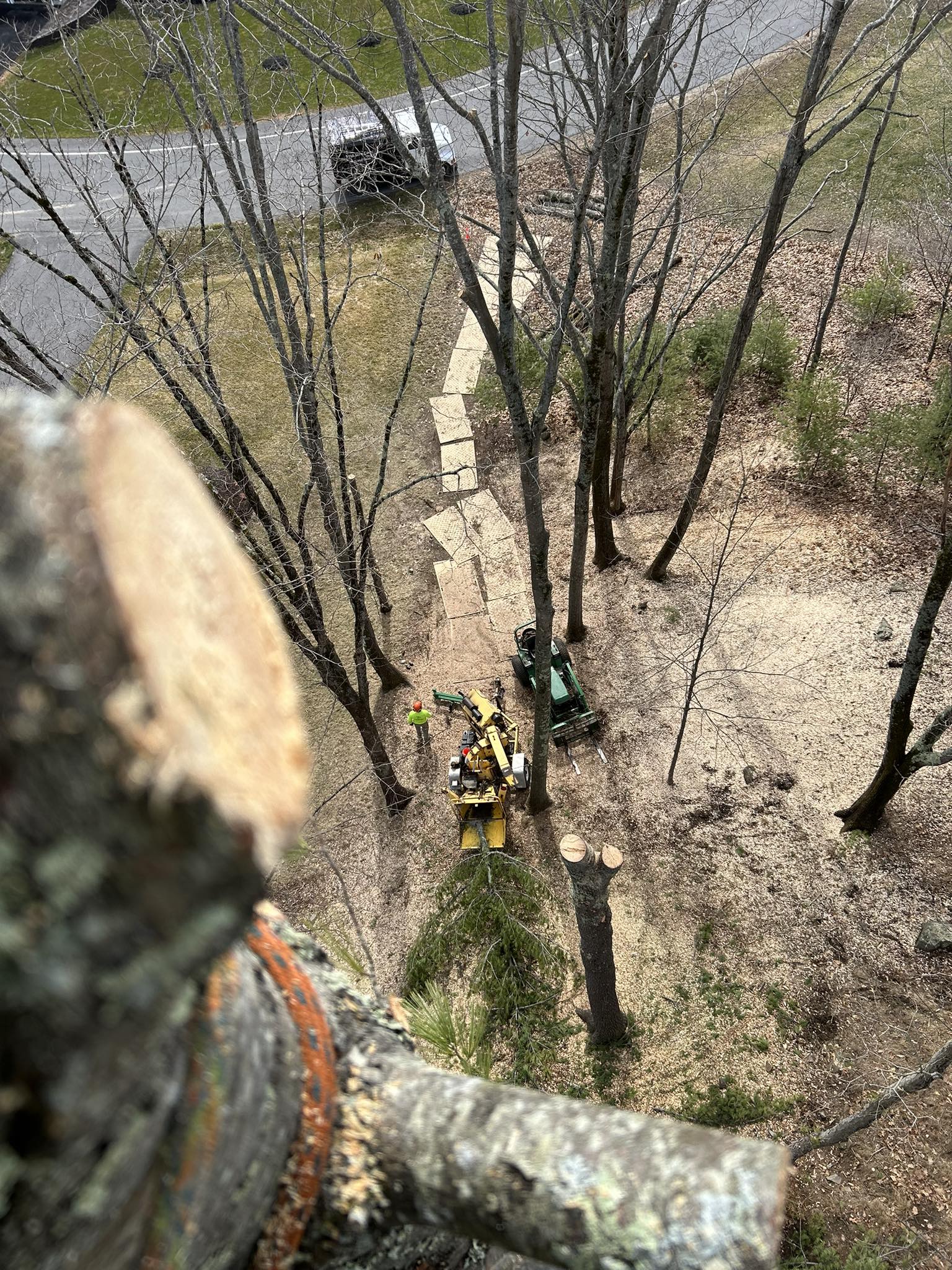 High aerial view looking straight down at a stone-patio backyard with a John Deere tractor, yellow chipper, and crew working below