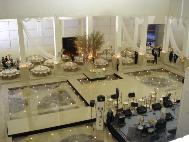Evento interior elegante con tarimas blancas, decoración con velas y flores blancas en disposición profesional
