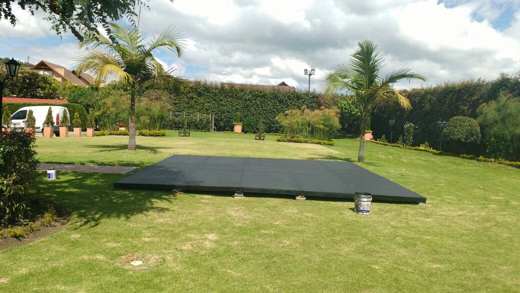 Tarima negra profesional instalada en jardín al aire libre con palmeras y jardín paisajístico