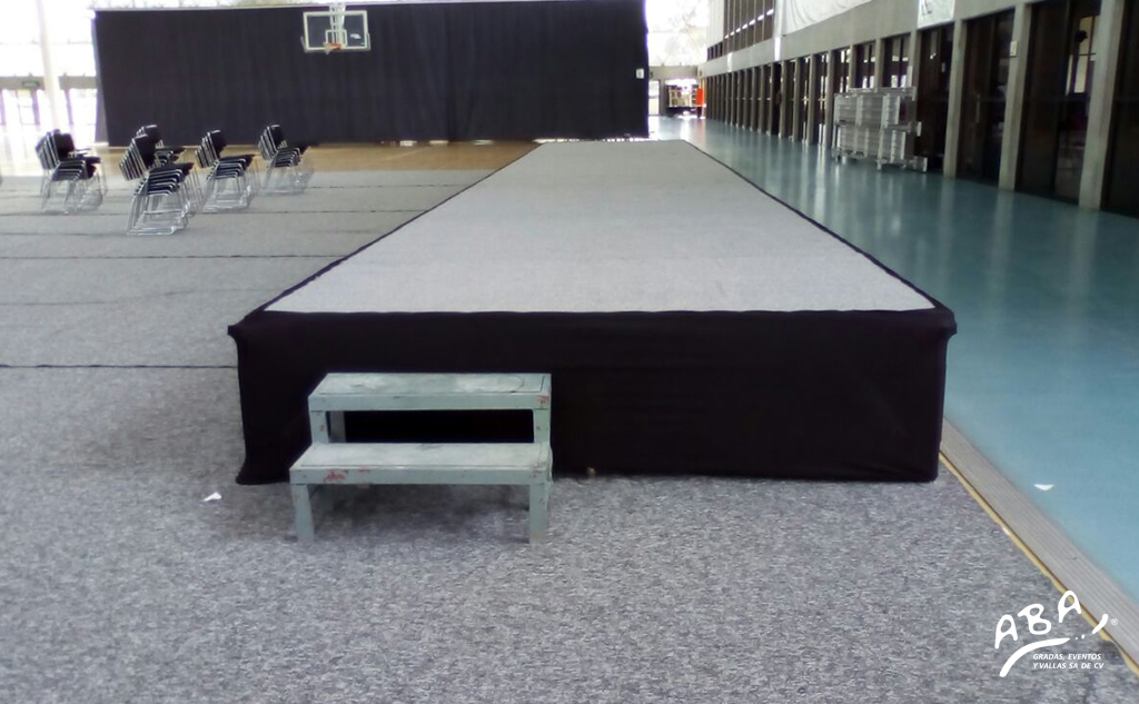 Tarima blanca elevada con falda negra en interior de salón para conferencia o evento deportivo